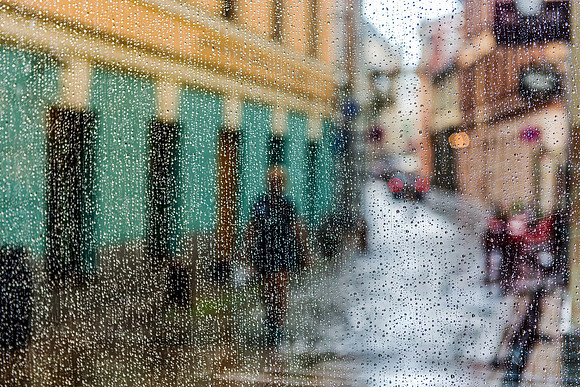 Riga: A rainy, atmospheric view of a cobblestone street through a textured glass window in Riga