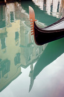 In Venice: The prow of a gondola is reflected in the green, shimmering canal water of Venice