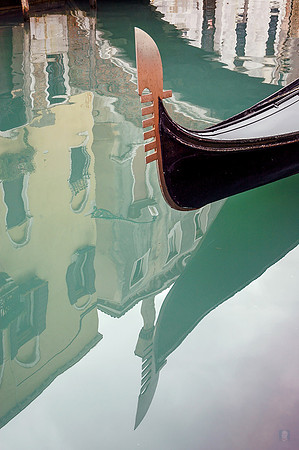 In Venice: The prow of a gondola is reflected in the green, shimmering canal water of Venice