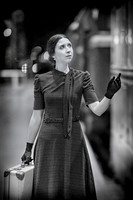 Retro-styled woman in polka dots stands beside a vintage train, gazing forward with hopeful anticipation