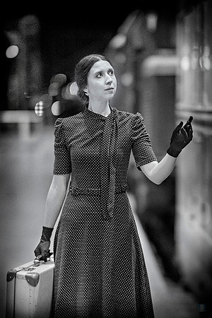 Retro-styled woman in polka dots stands beside a vintage train, gazing forward with hopeful anticipation