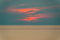 Preila A serene sunset with vibrant orange and pink clouds reflecting over calm coastal waters.