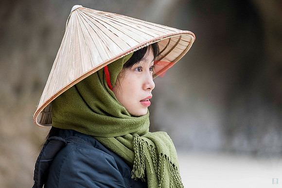 Profile portrait of Dzung wearing a traditional conical hat and dark jacket in Vietnam