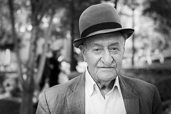 Grayscale portrait of an elderly man in Tehran wearing a bowler hat and jacket